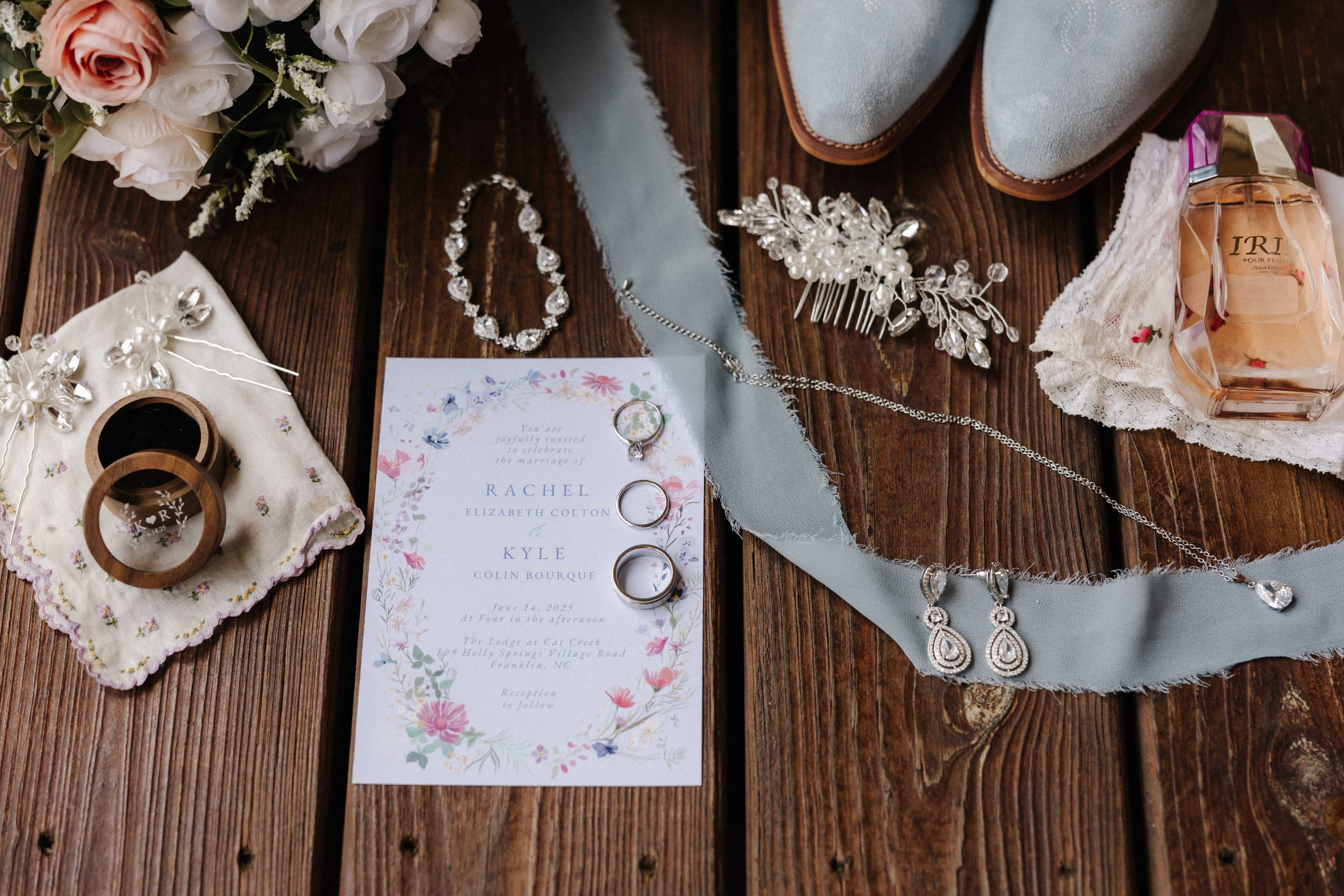 Flatlay of wedding rings, invitation, jewelry, and bridal details on rustic wood