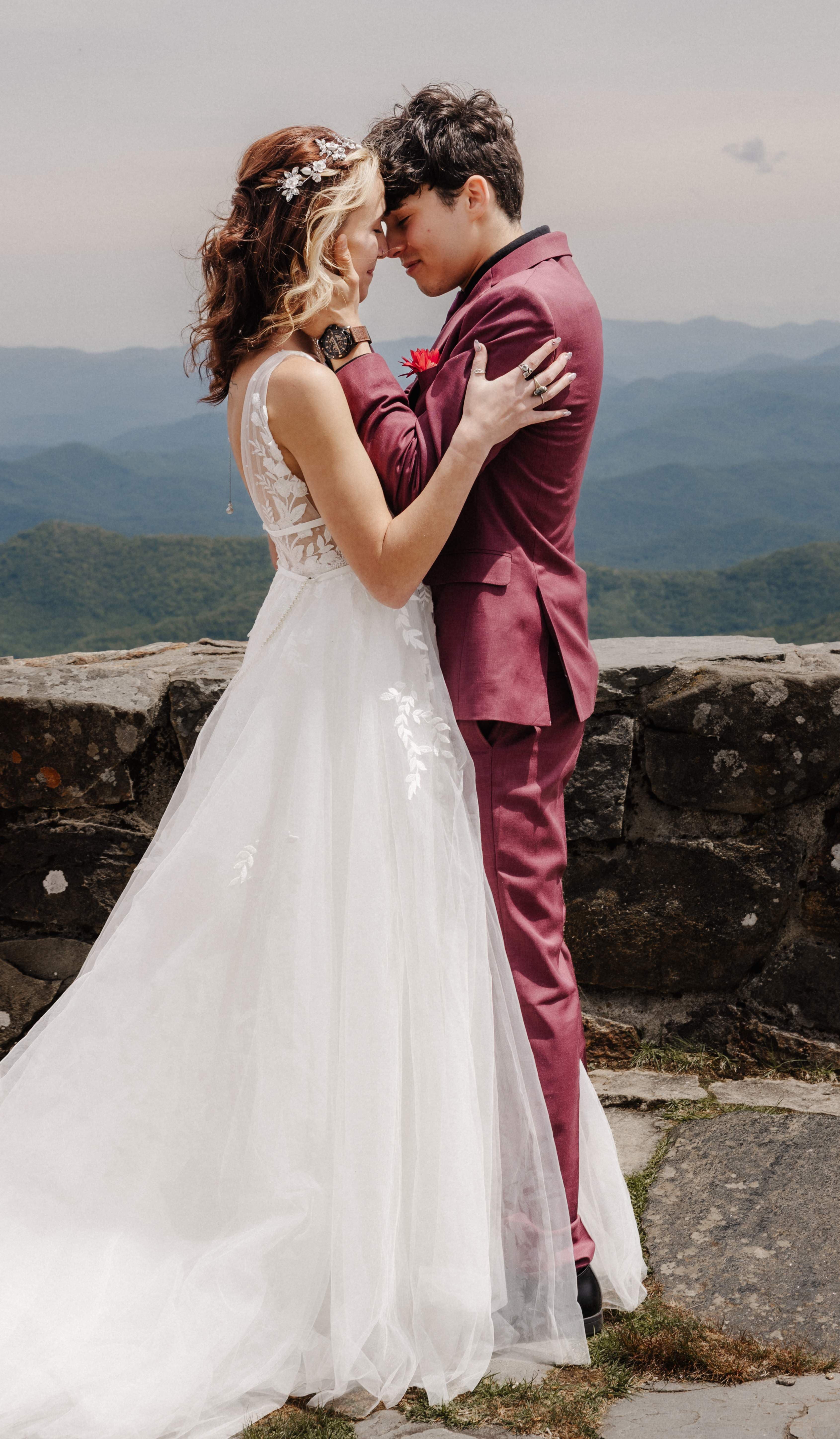 Bride and groom embracing forehead to forehead on a mountain overlook