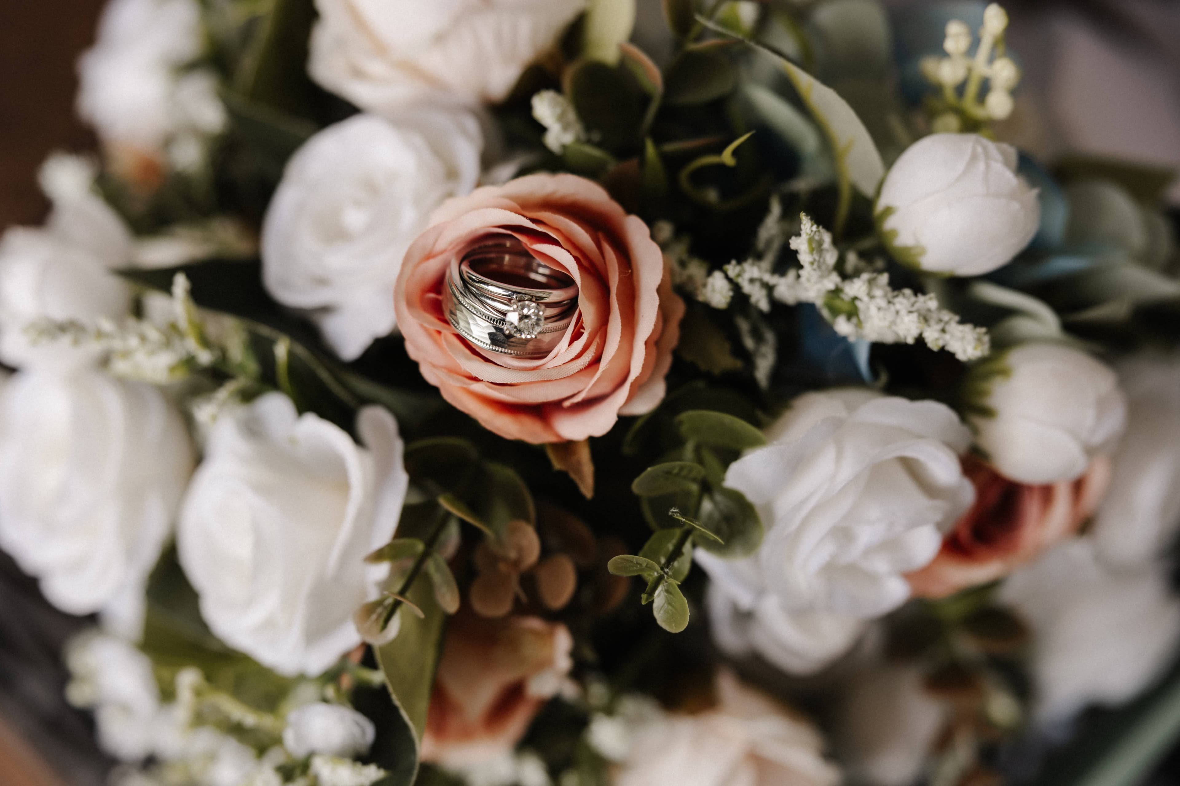 Wedding rings nestled in a rose surrounded by a bridal bouquet